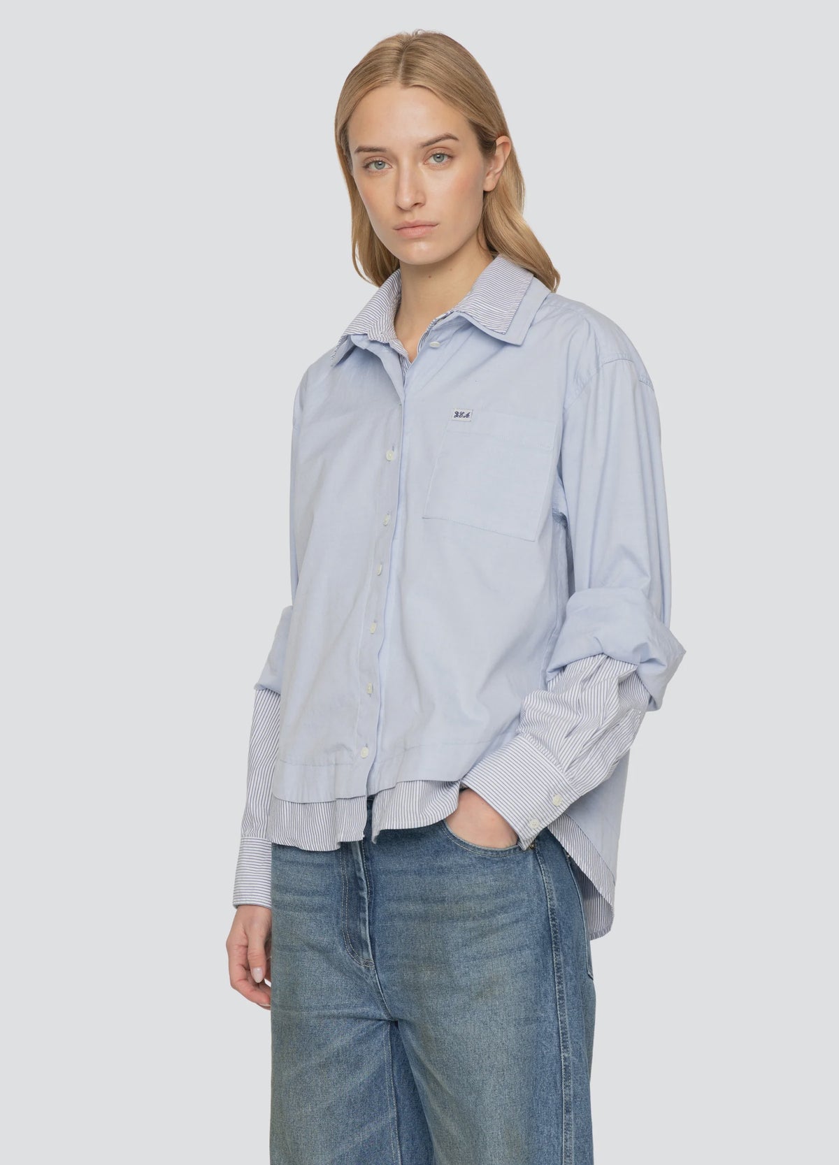Oversized light blue Zayna button down with layered striped hem and cuffs, worn with blue jeans.