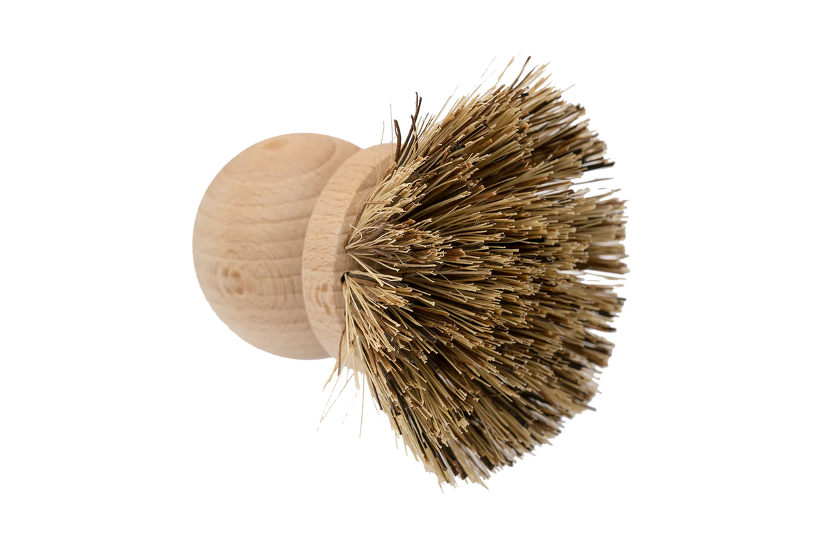 The Be Home Saucepan Brush is a round wooden kitchen brush with stiff, natural vegetable fiber bristles, inspired by timeless design and photographed against a plain white background.