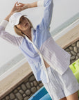 The Boyfriend Shirt by THE SHIRT styled casually with light shorts on a sunny beach, relaxed by colorful kayaks.