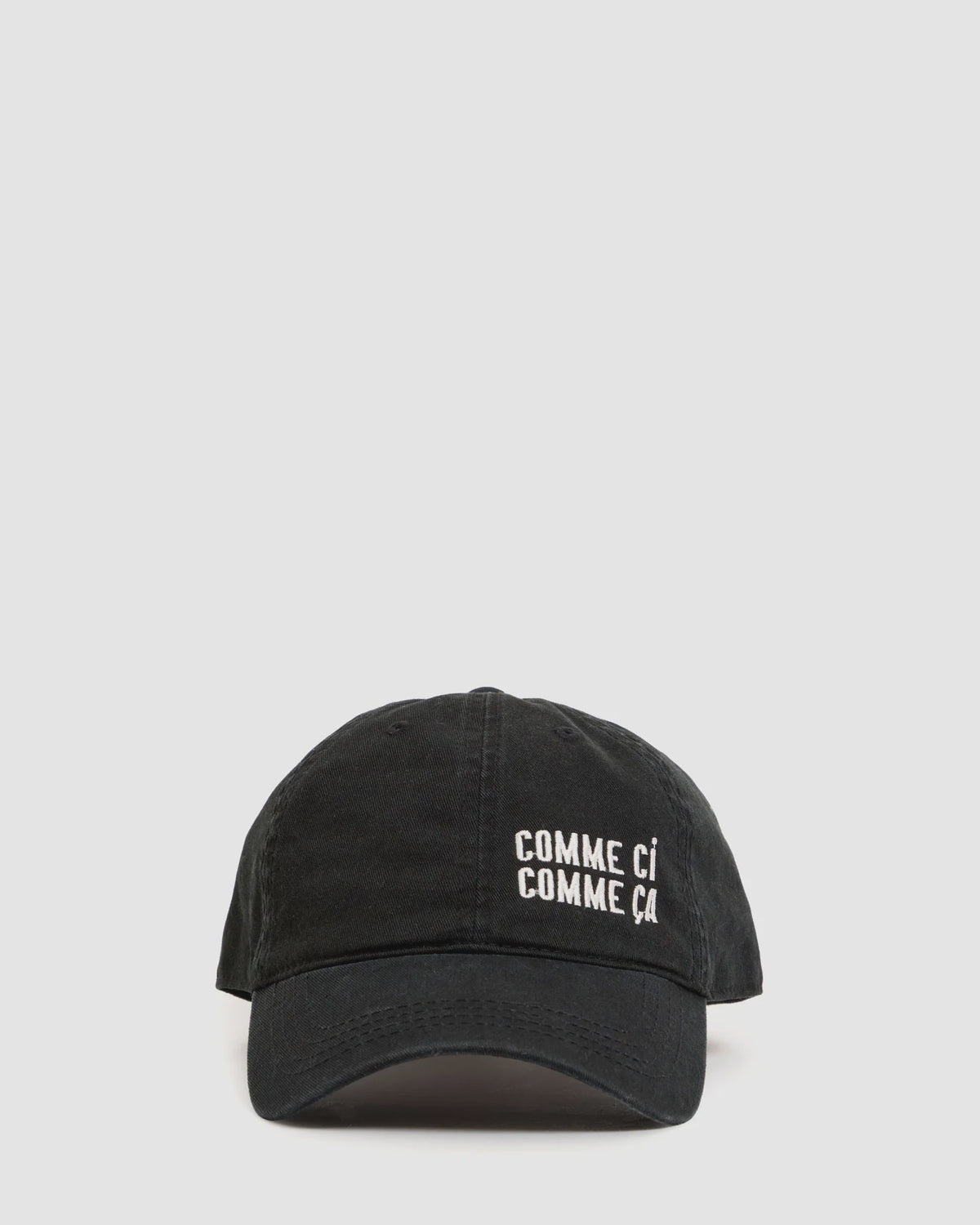 The Clare Vivier Baseball Hat - Comme Ci Comme Ca is a black cotton, adjustable hat with white embroidered "COMME CI COMME ÇA" text on the front, sliding metal closure, and one-size-fits-most fit. Shown on a plain light gray background.