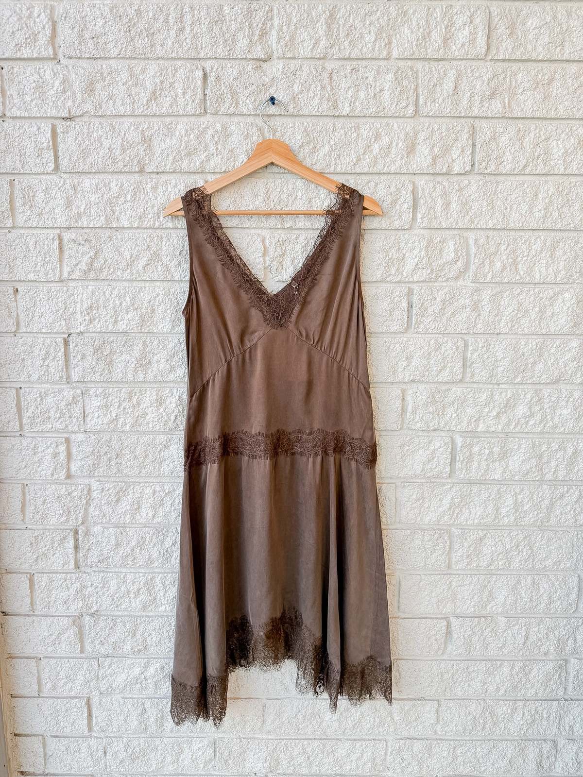Lace-trimmed brown cupro viscose slip dress by Xirena on hanger against white brick wall at Bungalow Furniture & Accessories.