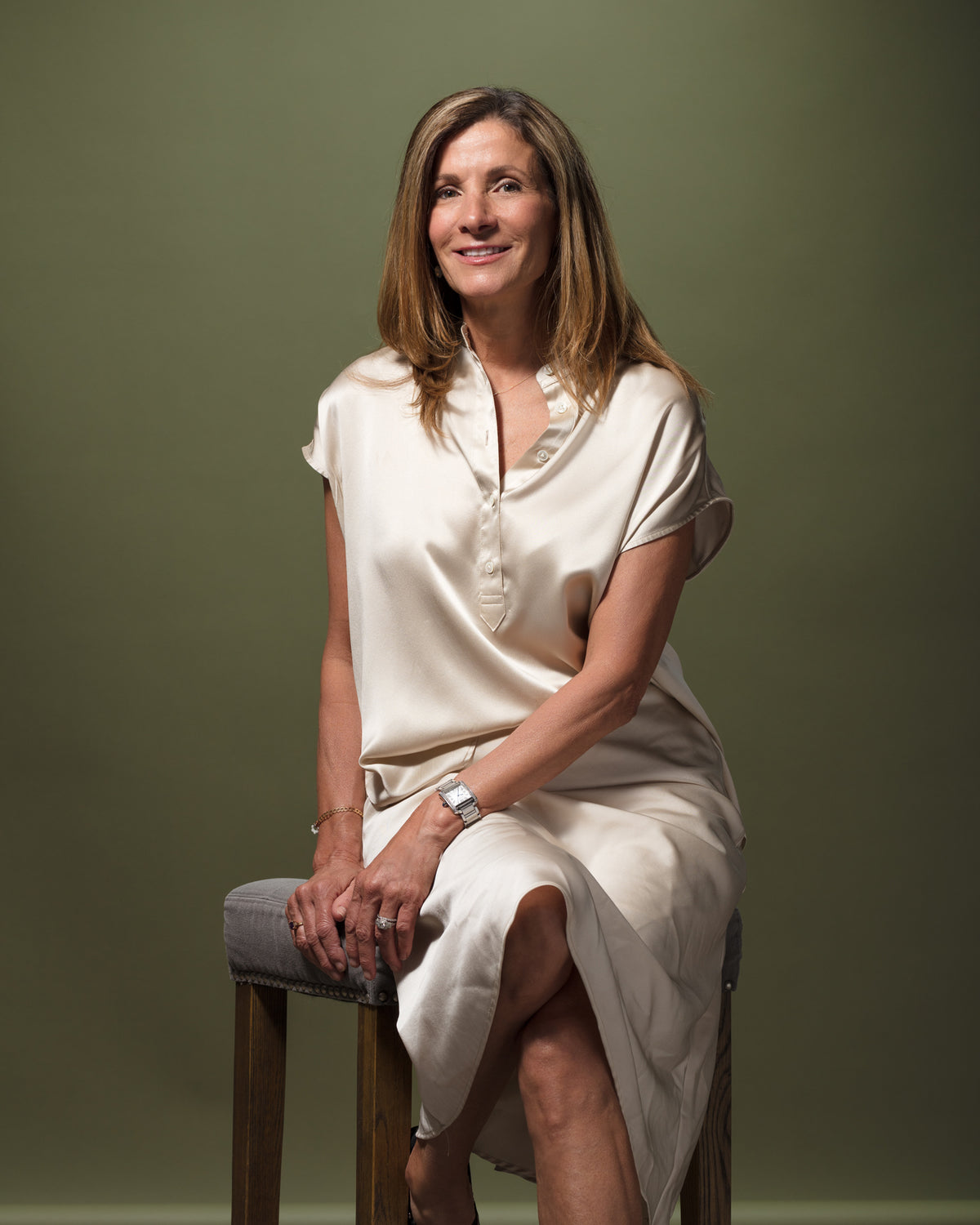 Cream dress styled in a relaxed, elegant setting with soft smiles and olive green backdrop, Bungalow Furniture & Accessories.