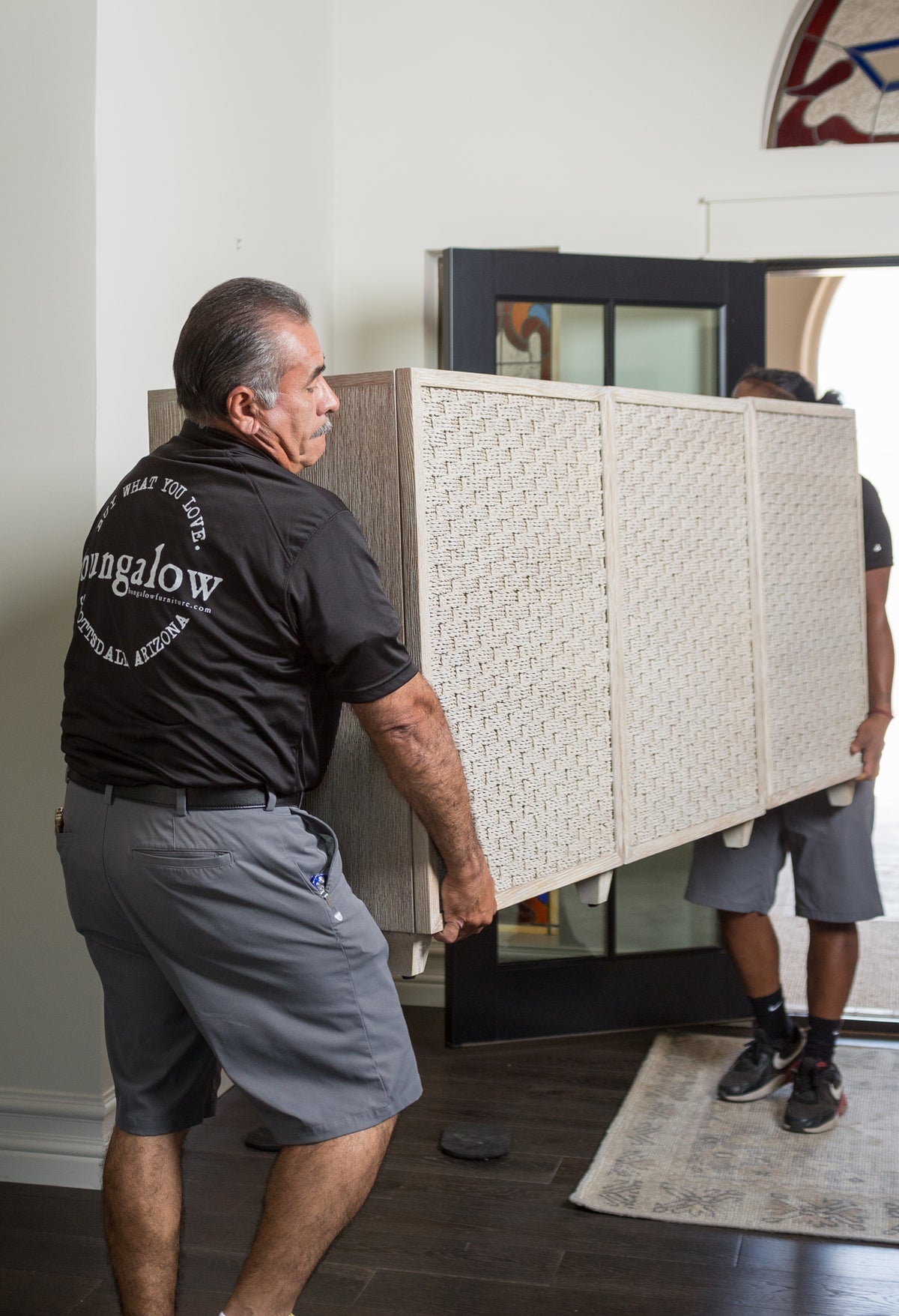 Movers carry a large wooden dresser across dark hardwood floors, showcasing Bungalow’s stylish home setting.