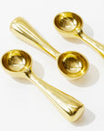 Three shiny, 100% food-safe Brass Dessert Scoops from Sir/Madam with a modern, rounded, and sleek handle design laid on a white background. The scoops are positioned at different angles, showcasing their reflective surface and making them a perfect addition to any kitchenalia collection.
