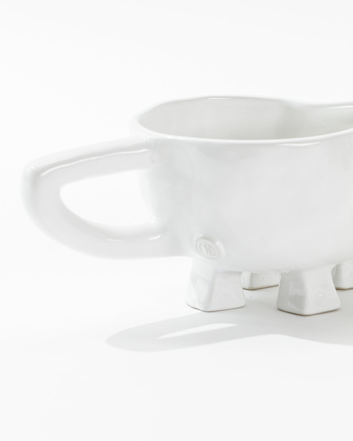 The Gravy Boat No. 151 by Montes Doggett is a quirky ceramic piece shaped like an animal with four leg-like feet and an oversized handle. Its minimalist design, with no distinctive features beyond the feet and handle, showcases the beauty of high-fired ceramic craftsmanship as it rests on a flat white surface.