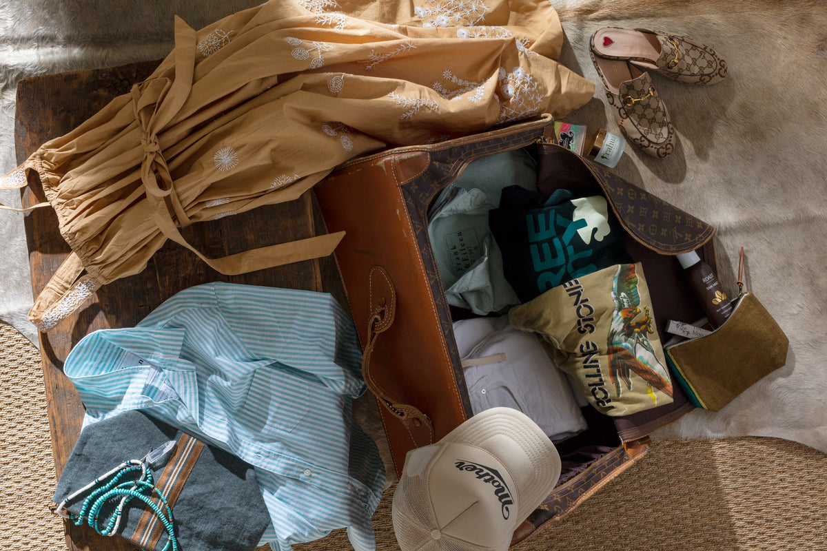 Open suitcase with stylish travel essentials on cowhide rug and wood floor, Bungalow Furniture & Accessories setting.