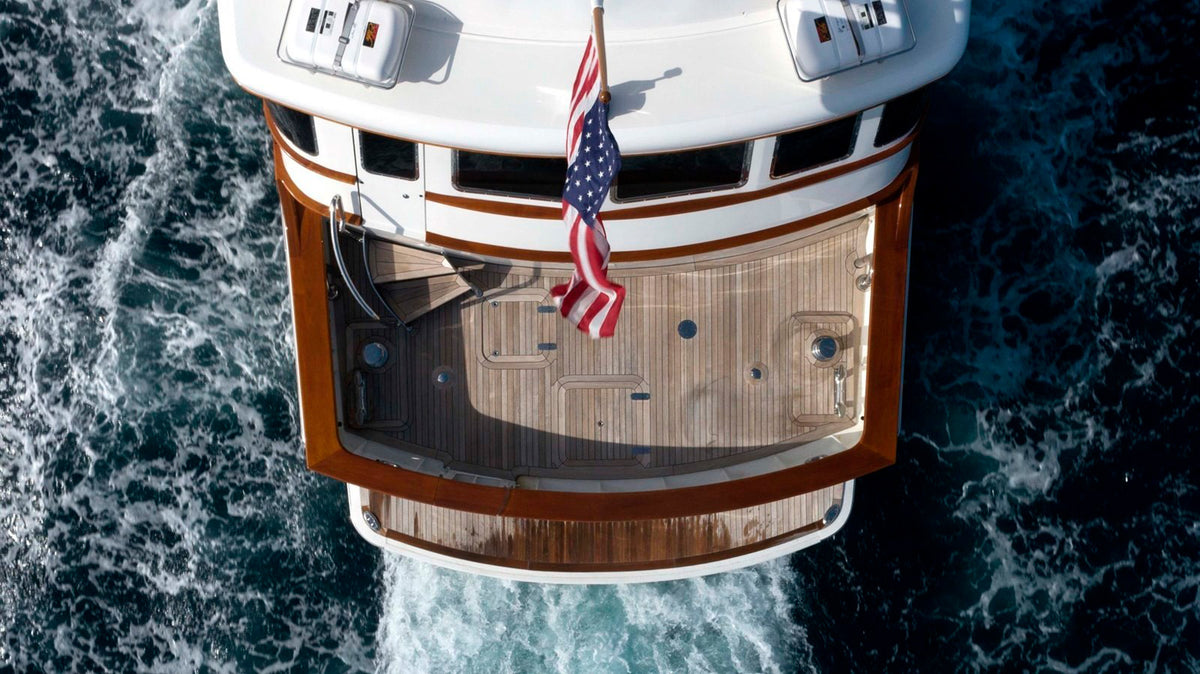 Boat with wooden deck and American flag cruising in blue ocean, showcasing coastal Bungalow Furniture style.
