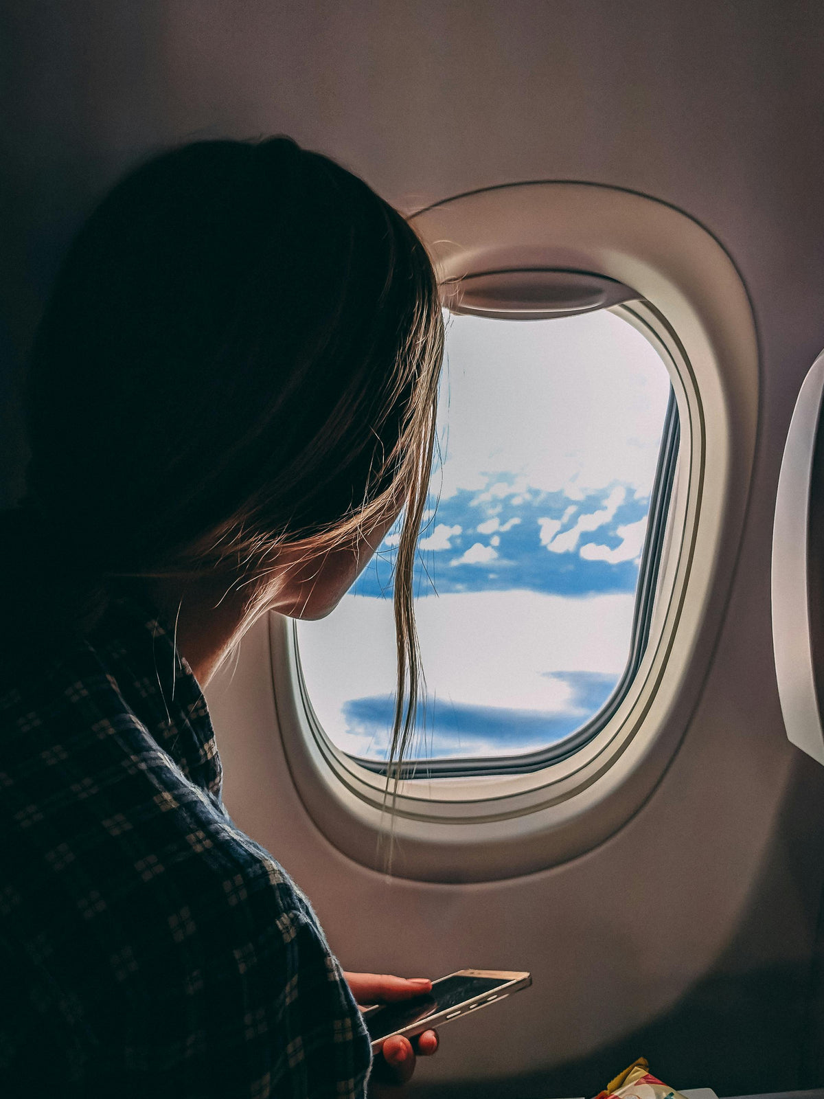 Modern travel style with a Bungalow carry-on by an airplane window, sunlit clouds and blue sky outside.