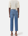 A person faces away, wearing CLOSED's Milo— a short-sleeved textured cream top with green trim, blue straight-leg sustainable denim jeans, and beige flat sandals—against a plain white background.