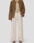 A woman stands against a plain light background wearing CLOSED Jayla Denim wide fit jeans, a brown suede jacket over a beige cardigan, black flip-flop sandals, and her hair is straight.