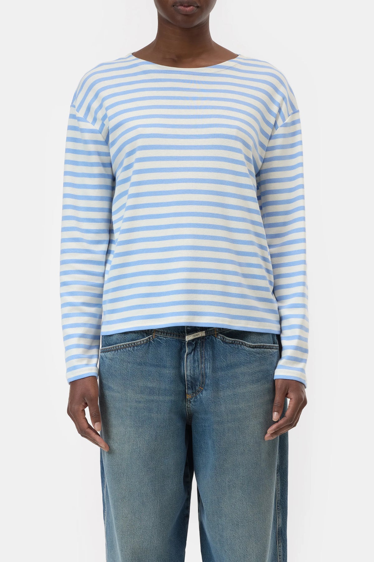 A person wears the CLOSED Basic Long Sleeve Tee in light blue and white stripes with blue jeans, standing against a plain white background.