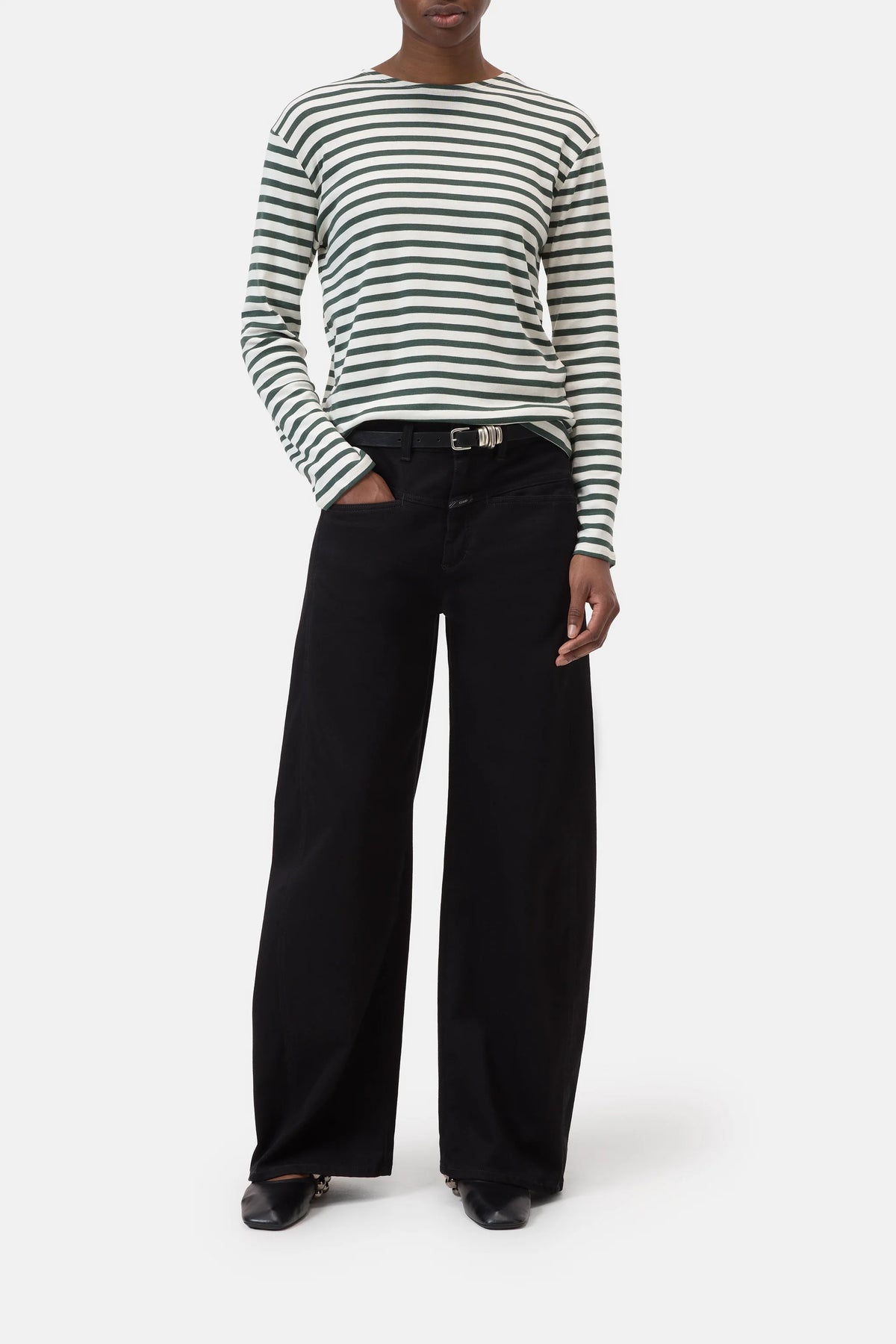 A person wears the CLOSED Basic Long Sleeve Tee in black and white stripes, paired with wide-leg black pants with a belt and black shoes, standing with one hand in their pocket against a plain white background.