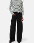 A person wears the CLOSED Basic Long Sleeve Tee in black and white stripes, paired with wide-leg black pants with a belt and black shoes, standing with one hand in their pocket against a plain white background.