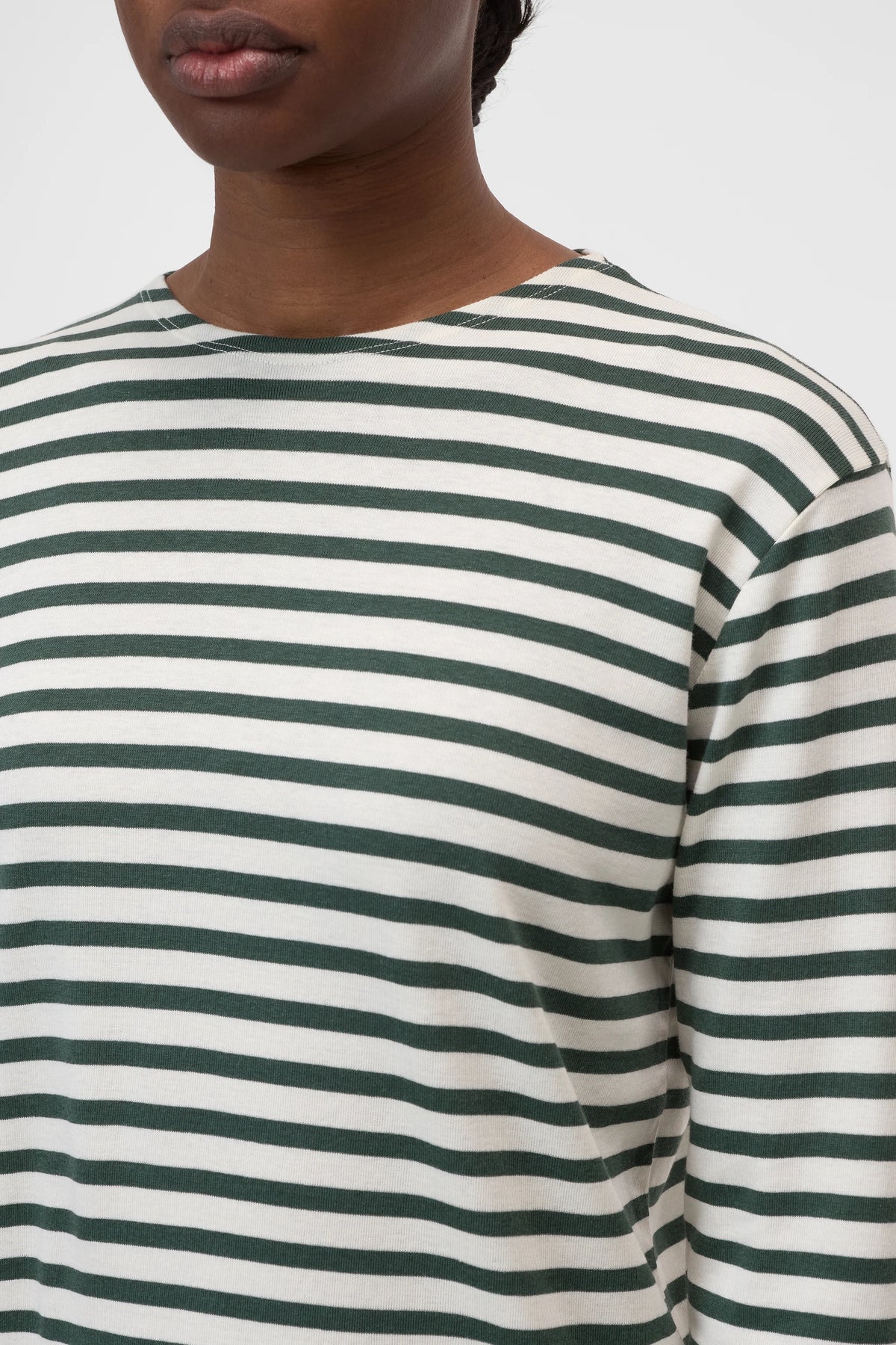 A person wearing CLOSED's Basic Long Sleeve Tee in white with dark green horizontal stripes, shown from shoulders to upper chest, stands against a plain light background.
