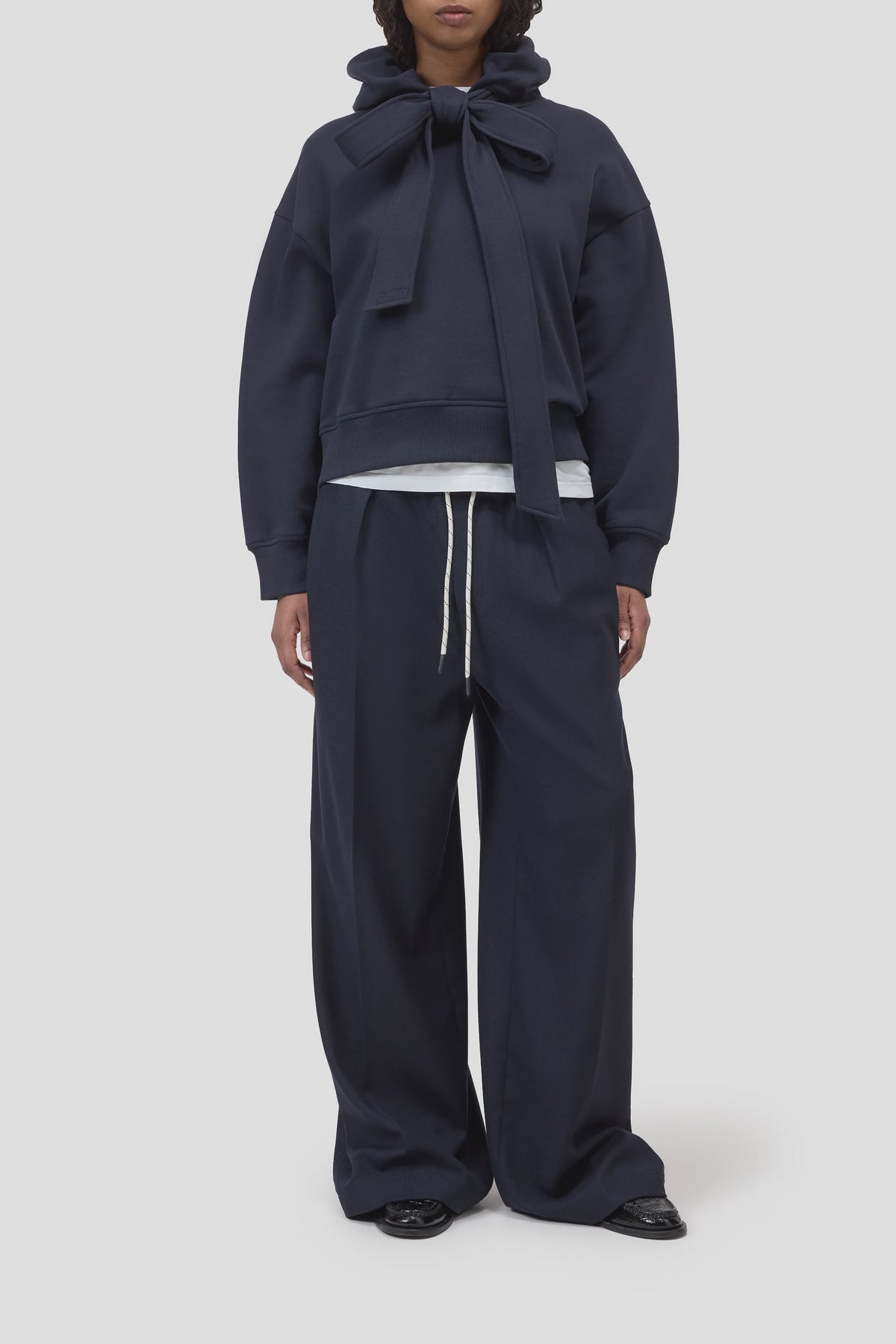 Navy Bow Tie Hoodie by CLOSED layered over white shirt with relaxed drawstring pants, casual modern look.