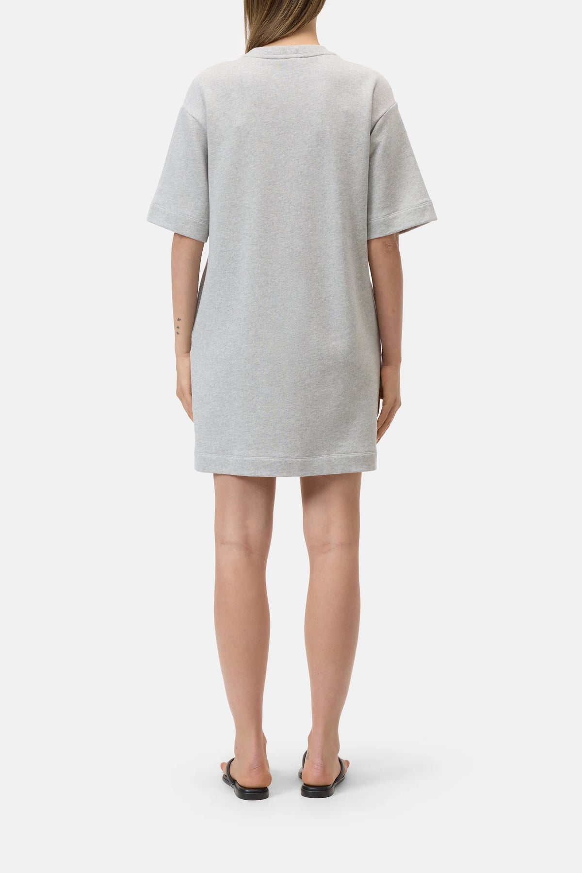A person faces away wearing the CLOSED Felpa Dress, a loose, short-sleeved light gray cotton piece made in Portugal, paired with black open-toe sandals against a plain white background.
