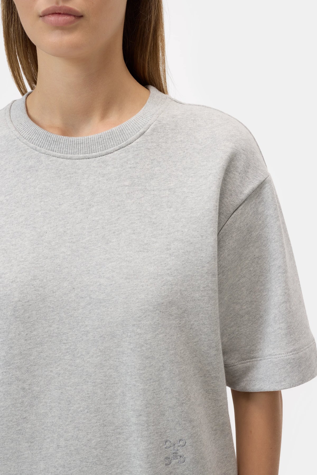 A woman wears the CLOSED Felpa Dress, a light gray, short-sleeve crew neck sweatshirt made of 100% cotton. She's shown from shoulders to mid-torso against a white background, with partially visible face and straight brown hair.