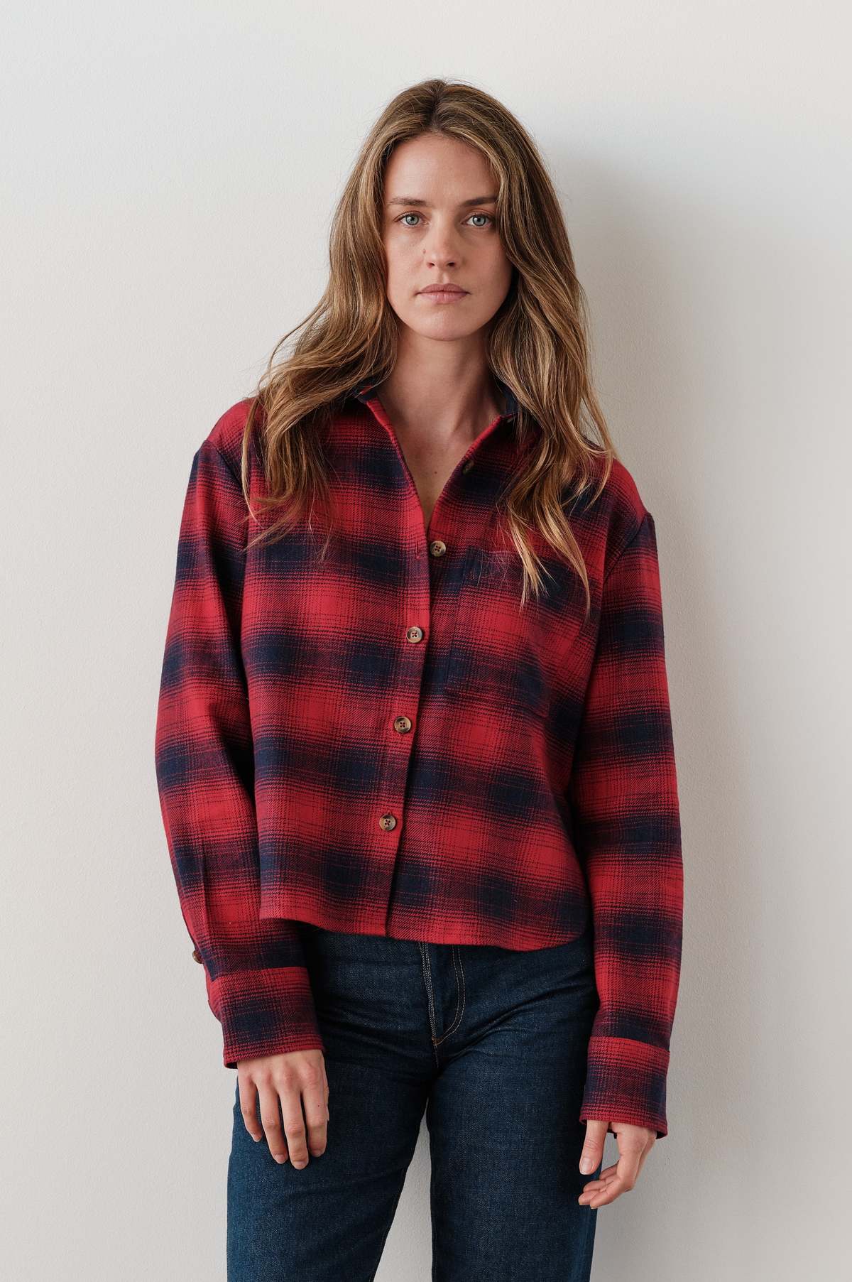 Red and black Cissa The FIELD Shirt styled with dark jeans, shown against a plain white wall for Bungalow Furniture.