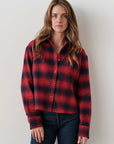Red and black Cissa The FIELD Shirt styled with dark jeans, shown against a plain white wall for Bungalow Furniture.