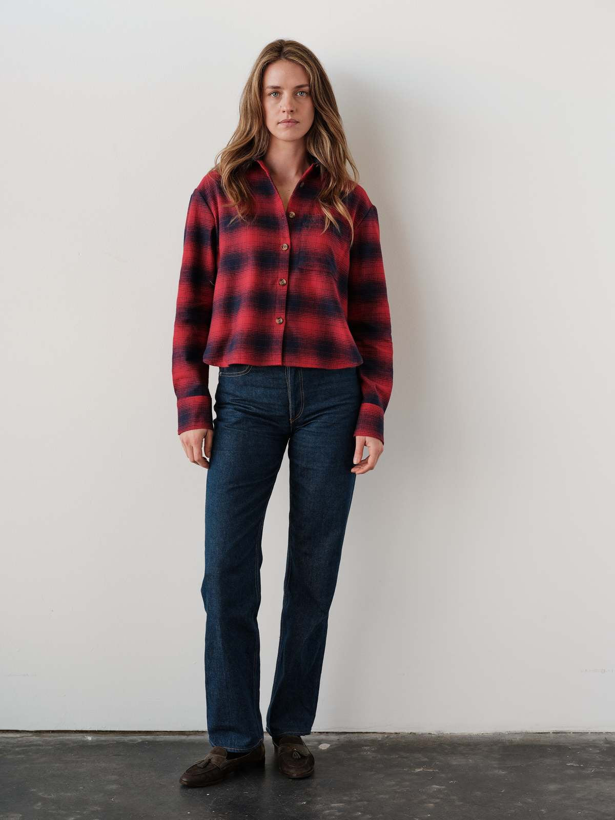 Cissa The FIELD Shirt in Redwood plaid styled with blue jeans, brown shoes, white wall backdrop.