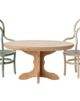 The Maileg Oval dining table by Maileg, paired with two bentwood chairs—one green, one cream—shows off its fine wooden quality and invites a cosy dinner party mood against a plain white background.