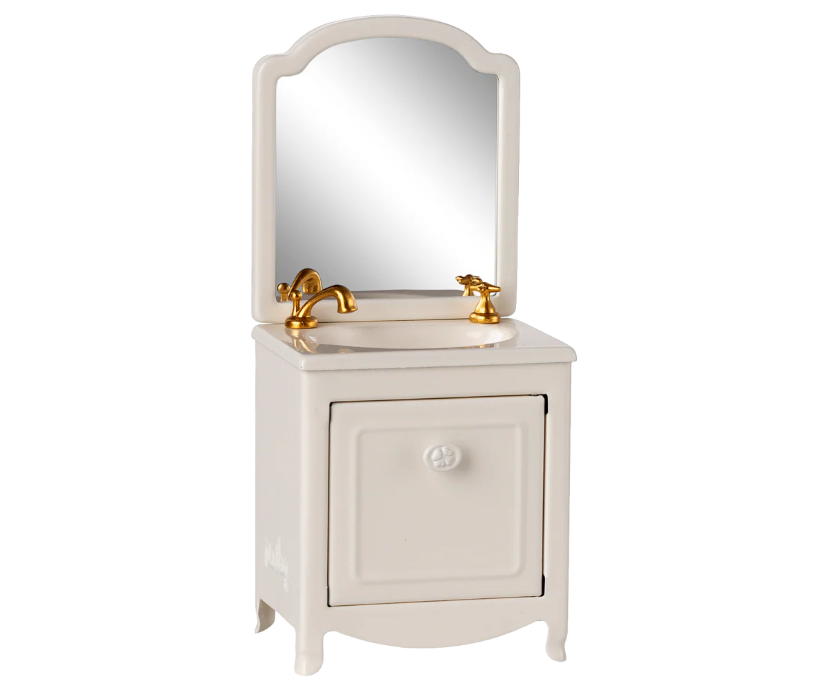 The Maileg Sink Dresser is a small, white farmhouse bathroom vanity with a cabinet door, gold faucet and handles, an attached mirror with rounded top corners, and a classic bathroom sink.