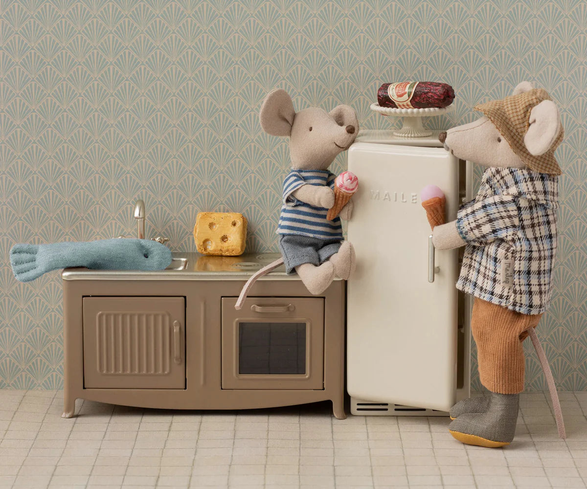 The Maileg Granddad Mouse by Maileg enjoys ice cream near a toy kitchen set with a fridge, sink, cheese, fish, and a small cake on the fridge—perfect for any playful mouse family.