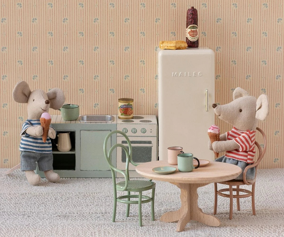 Two toy mice enjoy ice cream in a miniature kitchen; one sits on the Maileg Vintage Chair at the table, while the other stands by the stove. The cozy room features a fridge, mugs, and charming dollhouse furnishings.
