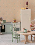 Two toy mice enjoy ice cream in a miniature kitchen; one sits on the Maileg Vintage Chair at the table, while the other stands by the stove. The cozy room features a fridge, mugs, and charming dollhouse furnishings.