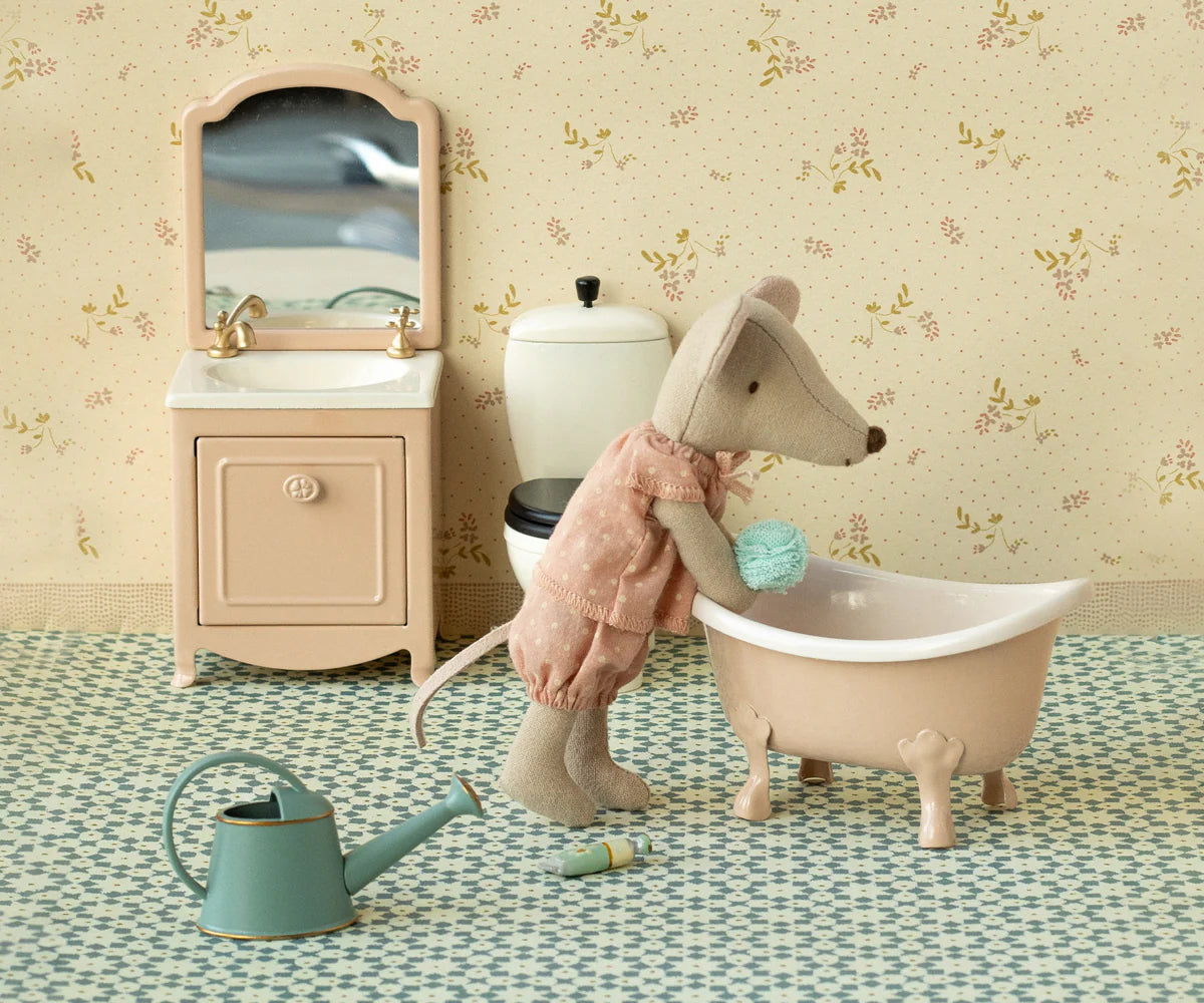 The Maileg Big Sister Mouse, Matchbox, wears pink pajamas and stands by a pink bathtub with sponge, sink and mirror, toilet, green watering can, bottle, and patterned floor—ideal to pair with soft bedding or matchbox toy accessories.