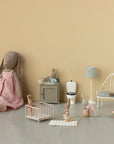 Maileg plush bunnies in different outfits are displayed in a miniature room with Maileg doll furniture, including the Maileg Playpen, crib, bed, cabinet, toilet, lamp, and tiny food items against a beige background.