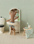Maileg mouse in a swim ring at a bathroom sink, featuring toothbrush set, towel, and toilet; playful decor by Maileg.