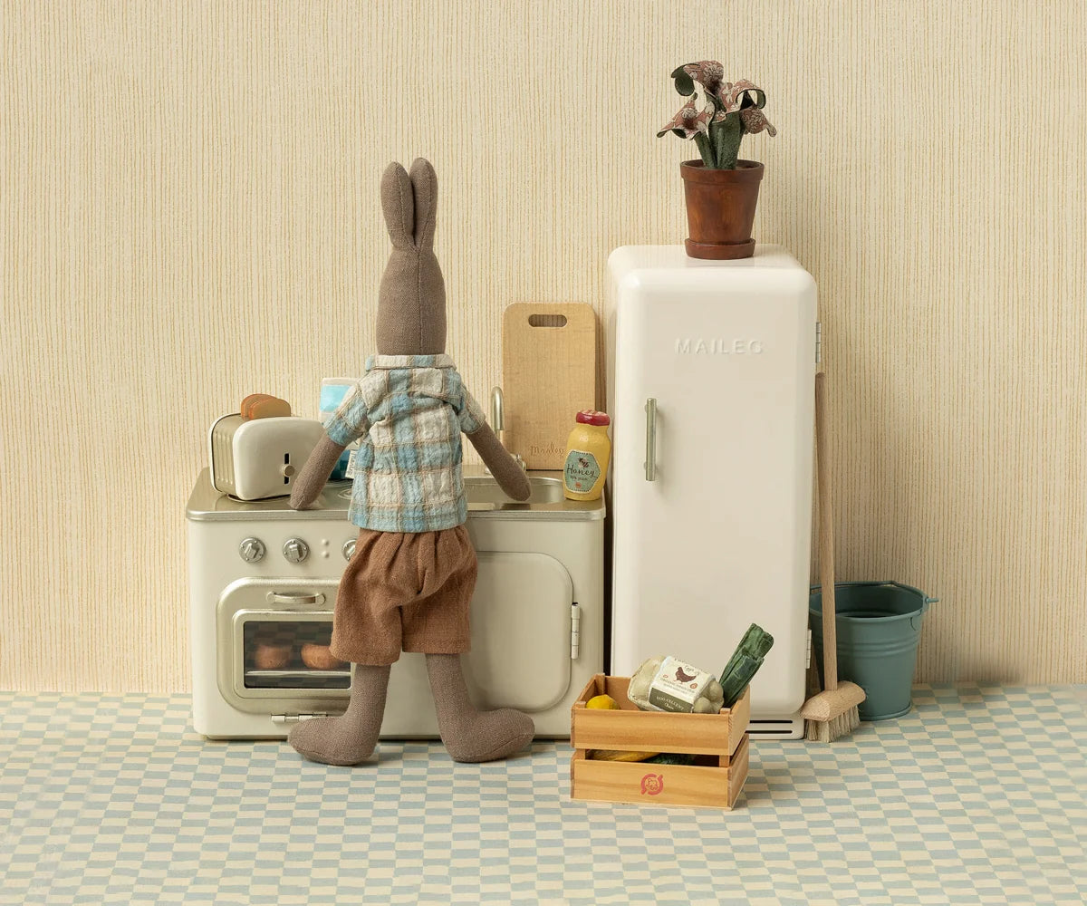 Maileg stuffed rabbit in a toy kitchen next to a Maileg toaster with toasted bread, playful and cozy setting.