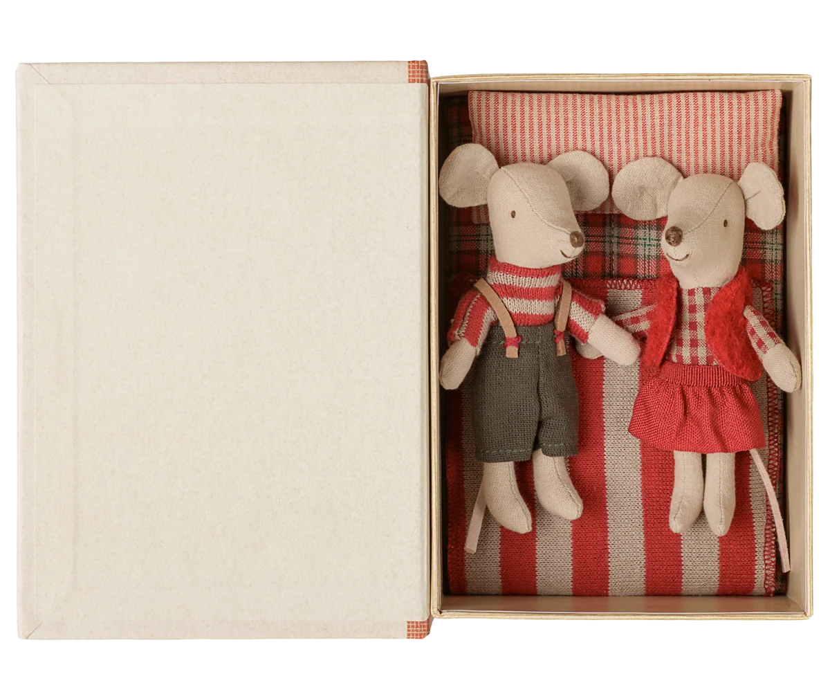 Maileg Christmas twin mice in winter clothing tucked in a cardboard box bed with a red-striped blanket.