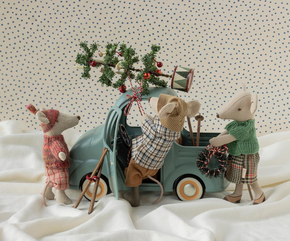 Three Maileg mice in festive winter outfits loading a Christmas tree onto a small blue toy truck.