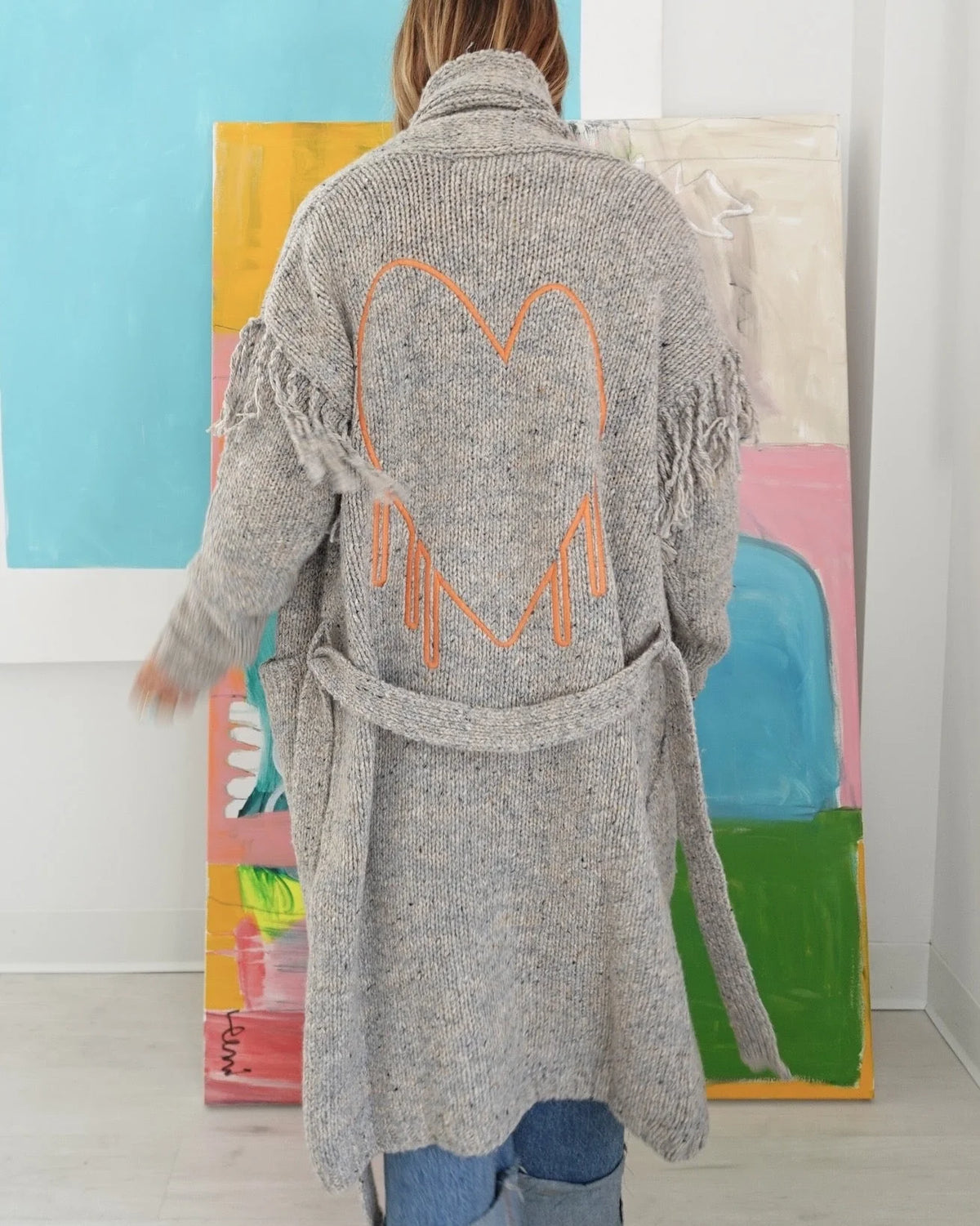Grey merino wool Cali Fringe Cardigan featuring fringe details and an embroidered orange heart on the back.