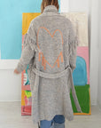 Grey merino wool Cali Fringe Cardigan featuring fringe details and an embroidered orange heart on the back.