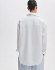 A person with dark hair in a bun, seen from behind, wears the Rag & Bone connie shirt and light blue and white striped pants while standing against a plain light background.