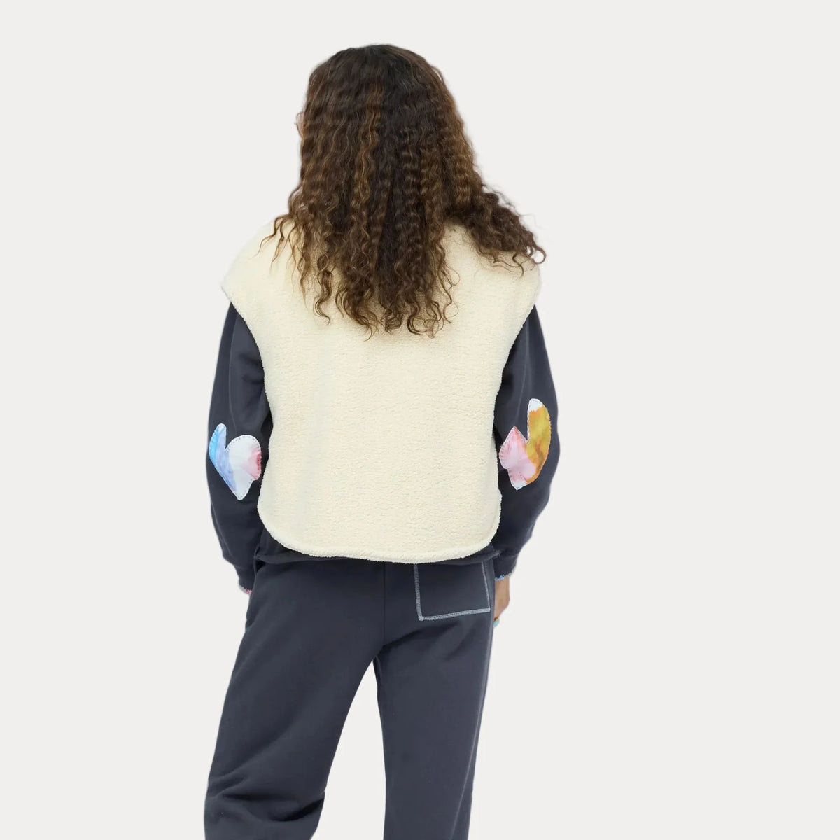 Kerri Rosenthal Coze Magoze Vest and dark patchwork-sleeve pants, shown from the back on a person with curly hair.
