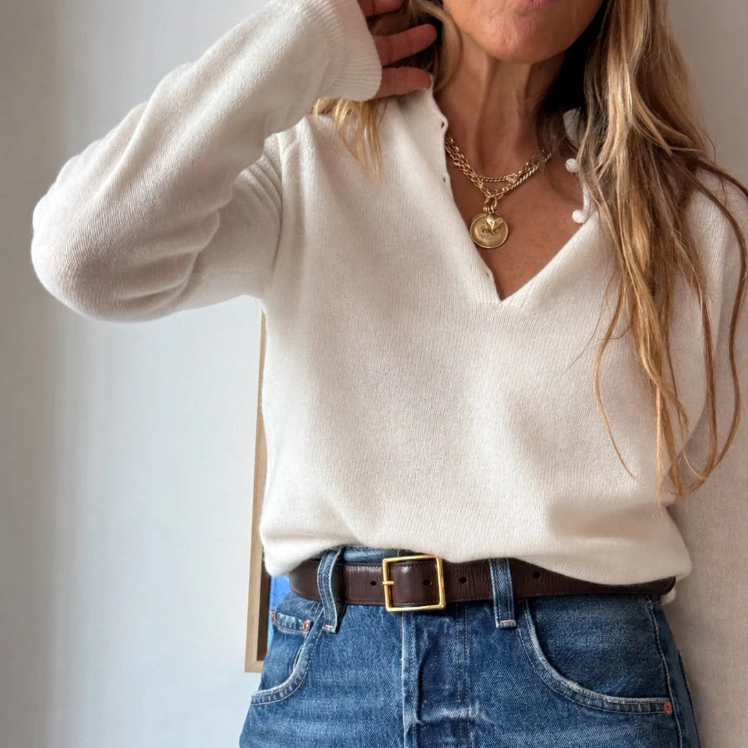 Cream Femme ruffle henley sweater tucked into blue jeans with a brown leather belt.