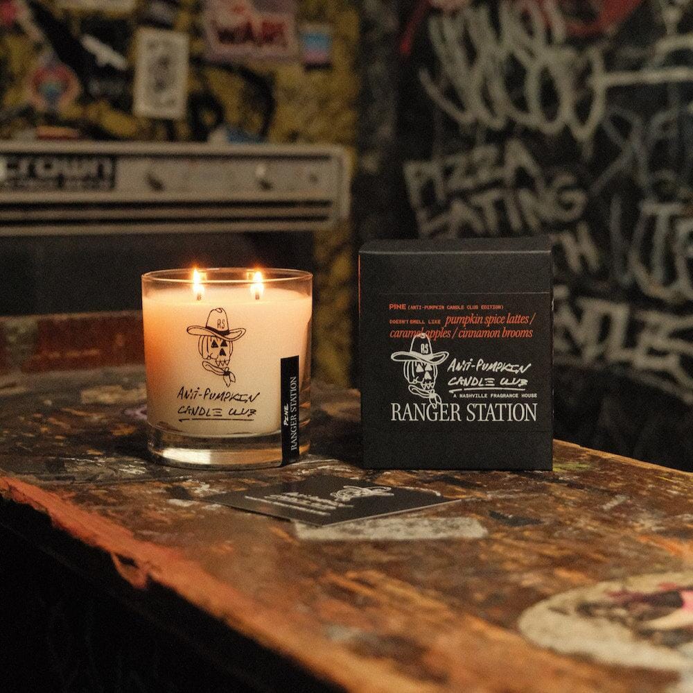 Faire Anti-Pumpkin soy candle in a glass jar next to its black box on a wooden table.