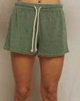 A person models Perfectwhitetee's Summer Loop Terry Sweat Shorts in green, featuring a white drawstring and elastic waistband, against a plain light background. Only the torso and upper legs are shown.