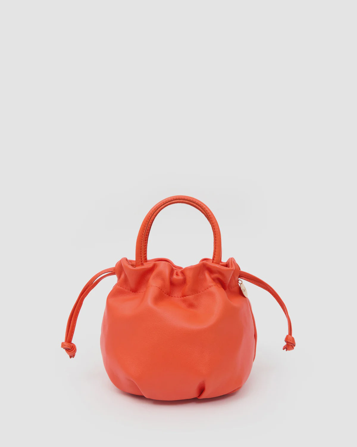 Bright orange Clare Vivier Emma Top Handle bag in Italian nappa leather with drawstring on light background.