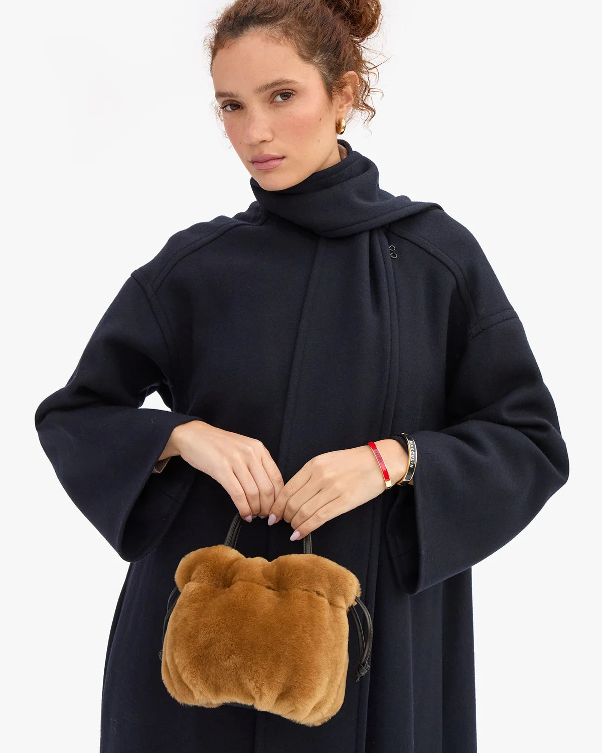 Brown shearling Clare Vivier Emma bag with drawstring closure held by a person in a navy wool coat.