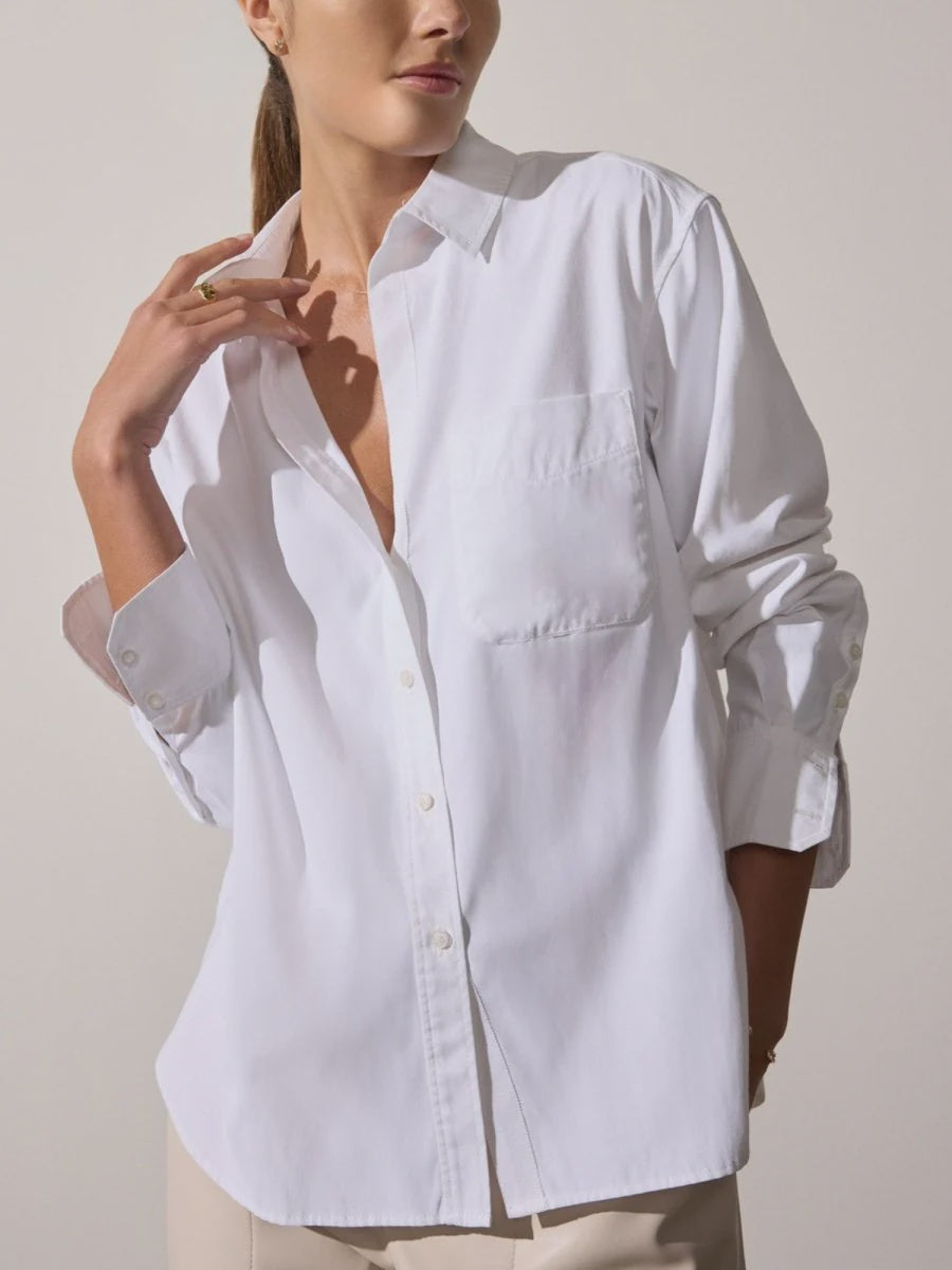 A woman stands against a plain background, wearing the BROCHU WALKER EVERYDAY SHIRT with long sleeves and a chest pocket, one hand touching her collar and the other in her pocket.