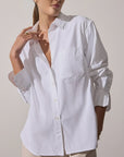 A woman stands against a plain background, wearing the BROCHU WALKER EVERYDAY SHIRT with long sleeves and a chest pocket, one hand touching her collar and the other in her pocket.