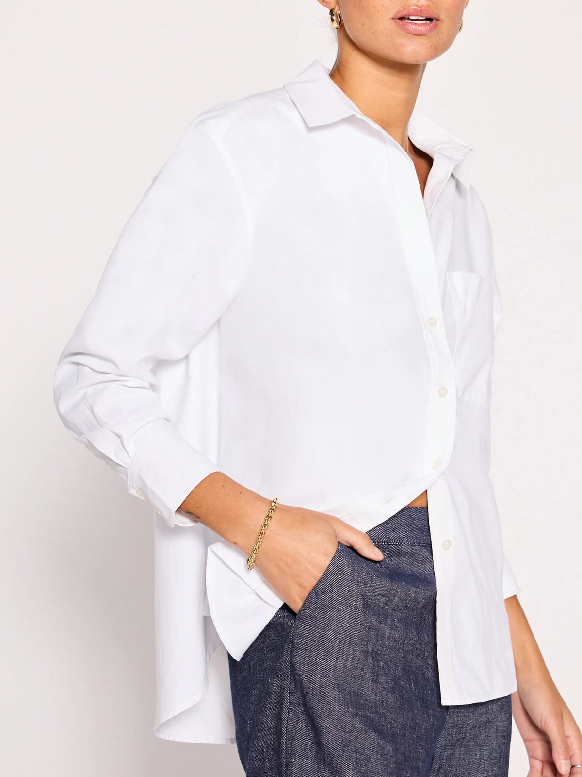 Someone wears the BROCHU WALKER EVERYDAY SHIRT in a relaxed fit with rolled sleeves, paired with dark blue jeans, one hand in their pocket and a gold bracelet on their wrist.