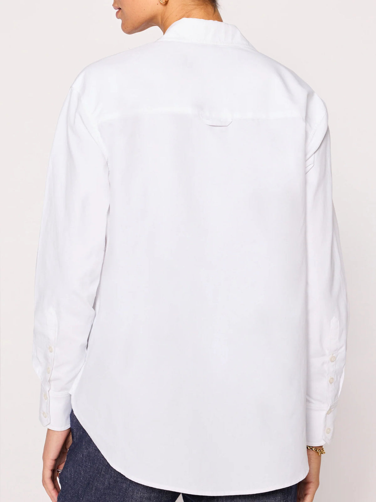 A person is seen from behind in the BROCHU WALKER EVERYDAY SHIRT, a relaxed-fit top with buttoned cuffs, paired with dark pants. The shirt drapes comfortably as they slightly turn their head to the side.
