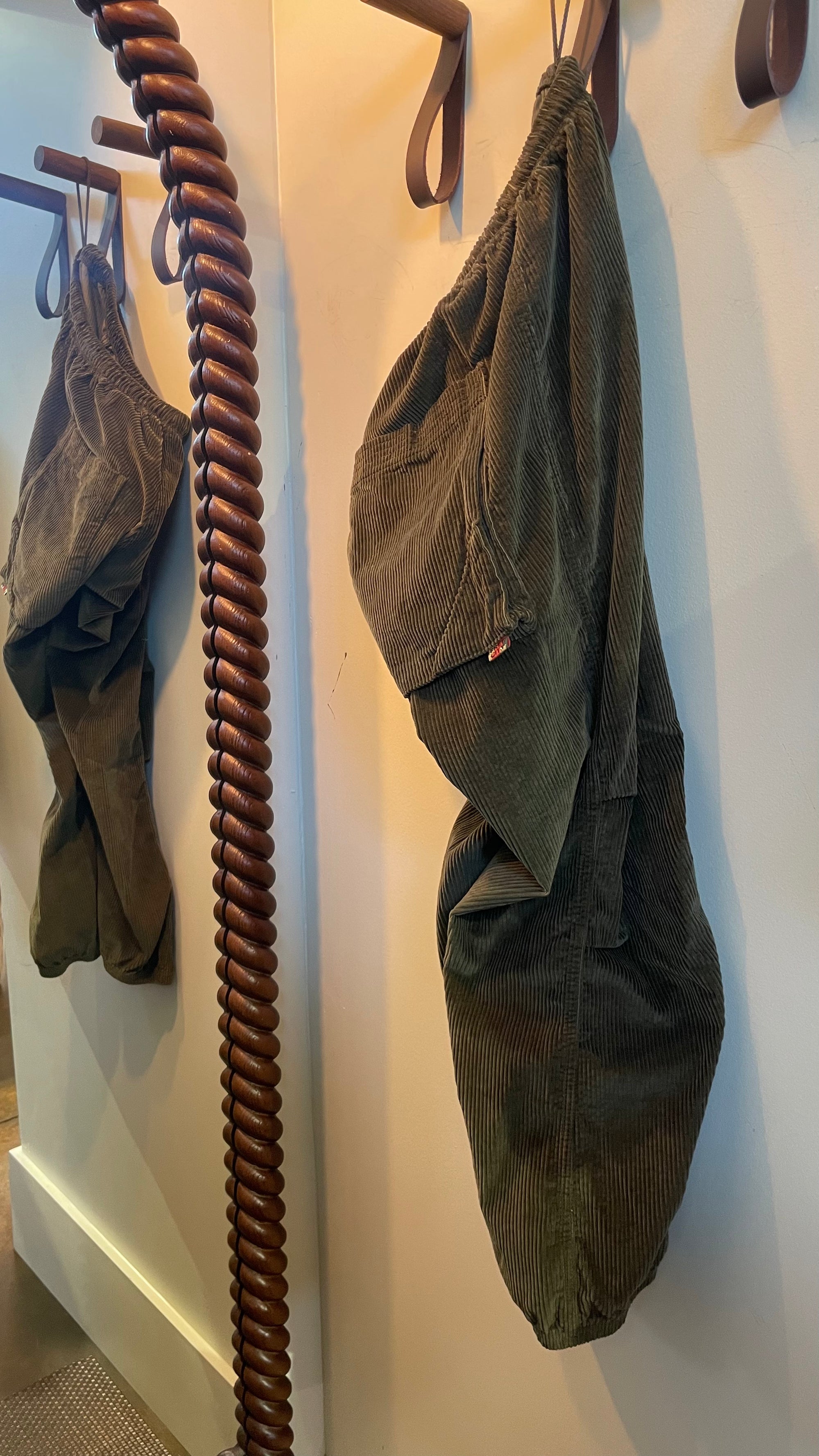 Olive green cashmere-blend corduroy baggy drawcord pants hanging on a twisted wooden pole.