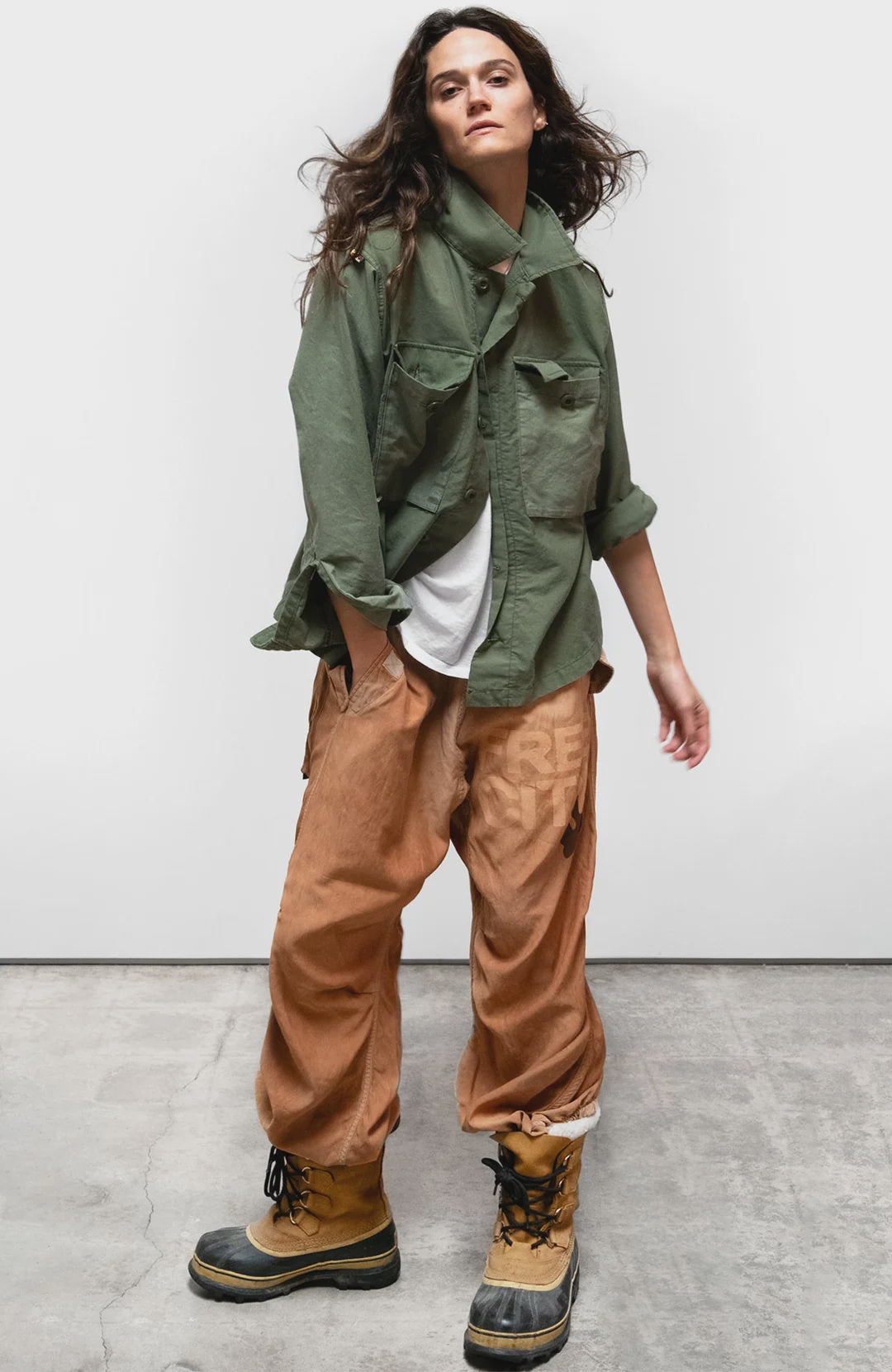 Tan satin Free City AirJump Pant 26 paired with a green sunfade jacket and boots on gray concrete.